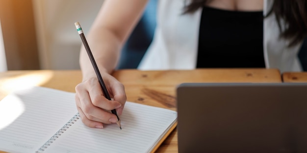 Gros plan sur les mains d'une femme avec un ordinateur portable, un ordinateur portable et un stylo prenant des notes au bureau d'affaires