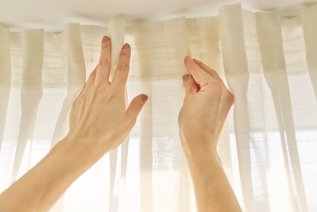 Gros plan des mains de femme rideau suspendu avec des crochets métalliques sur le rebord du plafond.