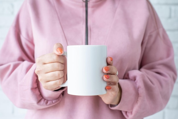 Gros plan des mains de femme tenant une tasse blanche pour la conception de maquettes