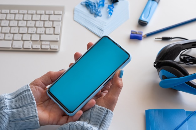 Gros plan sur les mains de la femme tenant un téléphone intelligent avec écran bleu. Couleur bleue sur les accessoires