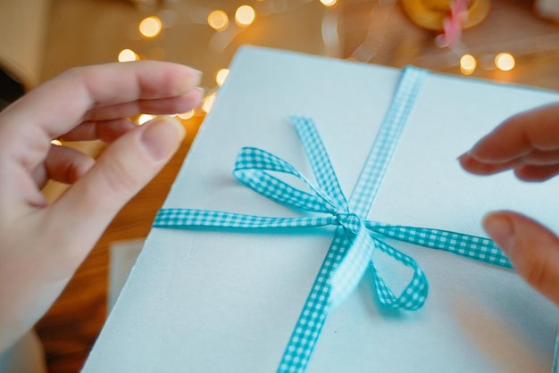 Gros plan des mains des femmes et du ruban à carreaux bleu sur une boîte cadeau blanche surprise de noël ou d'anniversaire