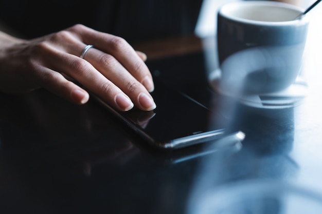 Gros plan des mains des femmes tenant un smartphone, femme utilisant un téléphone portable pendant la pause-café.