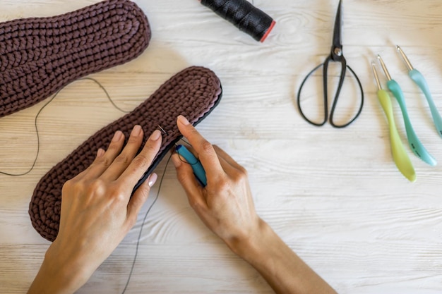 Gros plan des mains des femmes à tricoter des pantoufles en laine à coudre semelle de connexion et fil utiliser une aiguille à fils