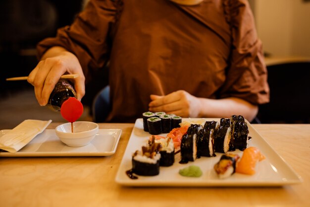 Photo gros plan sur les mains des femmes versez la sauce soja pour les sushis. personne méconnaissable au café