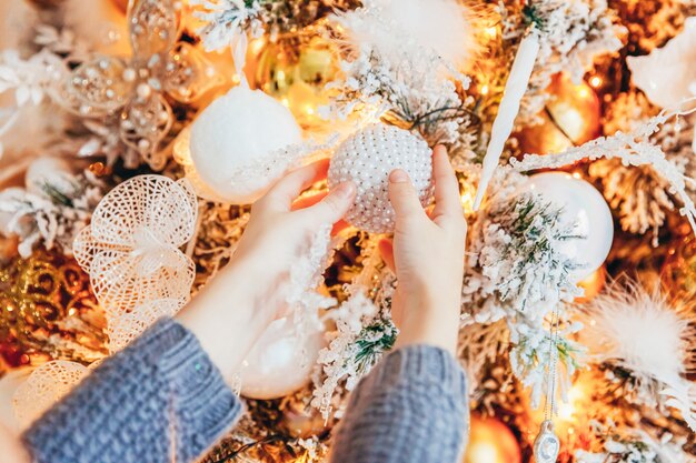 Gros plan des mains de fille décorant l'arbre de Noël à la maison