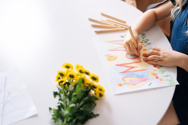 Gros plan des mains d'une fille méconnaissable dessinant avec des crayons de couleur à la table