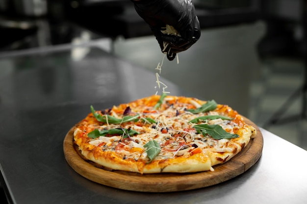 Gros plan des mains gantées du chef saupoudrant de fromage râpé sur la pizza finie