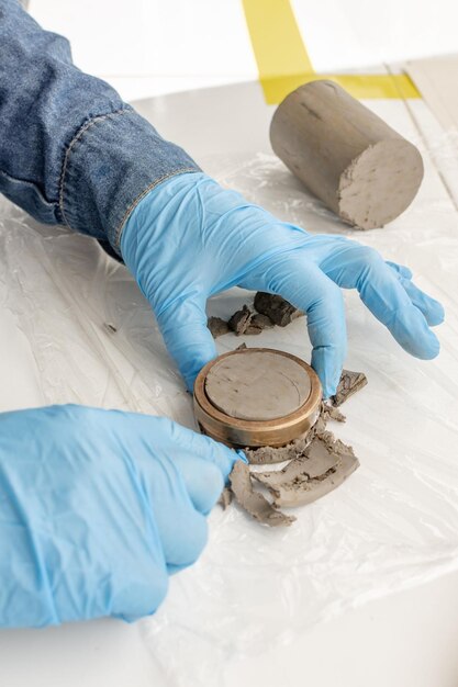 Gros plan des mains avec des gants bleus tenant un anneau de cuivre avec de l'argile pour faire des tests de laboratoire