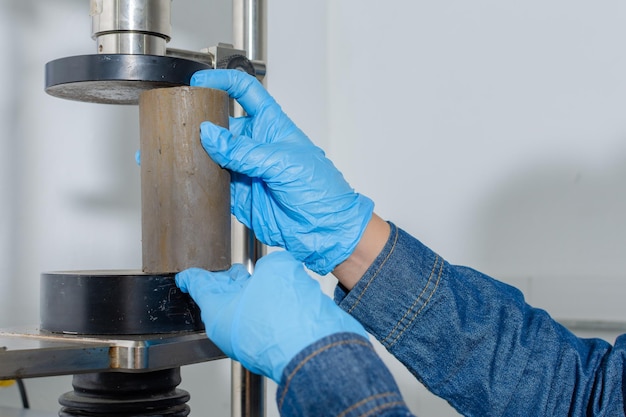 Gros plan des mains avec des gants en latex bleu plaçant un cylindre d'argile dans une machine d'essai géologique