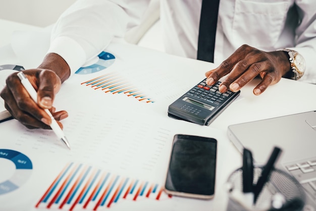 Gros plan sur les mains d'un homme d'affaires africain travaillant sur une calculatrice dans le bureau moderne.