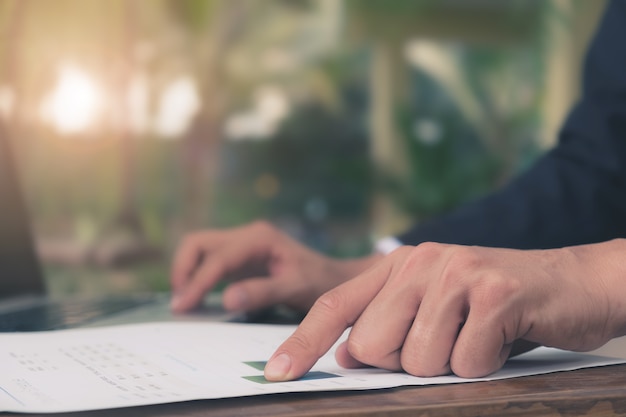 Gros plan Les mains de l&#39;homme d&#39;affaires indiquent le travail papier et travaillent avec un plan financier et un ordinateur portable sur le bureau en bois au bureau.