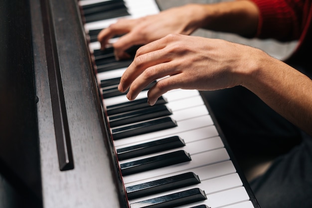 Gros plan des mains d'un homme méconnaissable jouant au piano dans un studio d'enregistrement à domicile