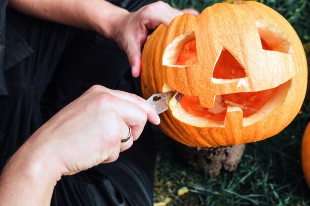 Un gros plan de mains d'homme qui coupe avec un couteau une citrouille alors qu'il prépare un jack-o-lantern.