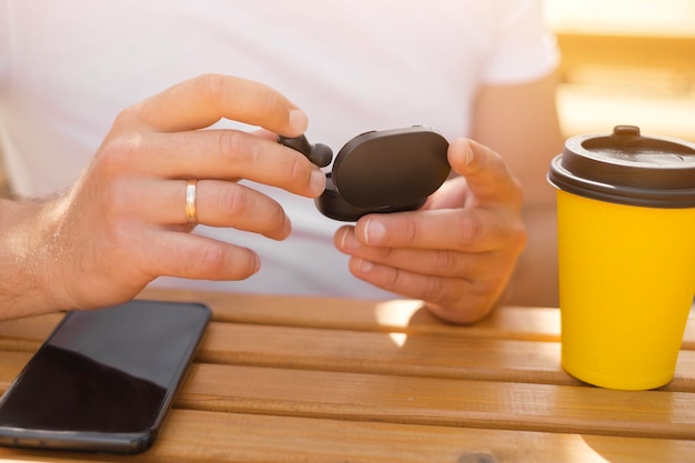 Gros plan sur les mains d'un homme sortant de la boîte de petits écouteurs noirs sans fil