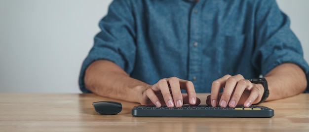 Gros plan des mains de l'homme tapant sur le clavier de l'ordinateur sur une table en bois au bureau à domicile ou sur le lieu de travail.