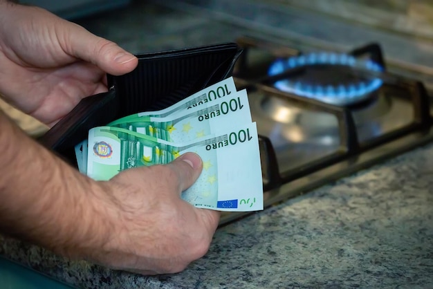 Gros plan des mains des hommes avec un sac à main et des billets en euros sur le fond d'une cuisinière à gaz