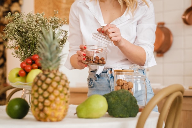 Gros plan des mains de l'hôtesse tenant des noix dans un bocal et des légumes fruits couchés au premier plan sur la table de cuisine