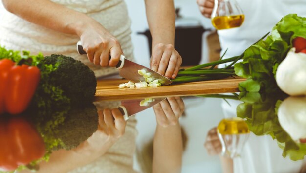 Gros plan sur des mains humaines cuisinant dans la cuisine. Mère et fille ou deux amies coupant des légumes pour une salade fraîche. Concepts d'amitié, de dîner en famille et de style de vie.