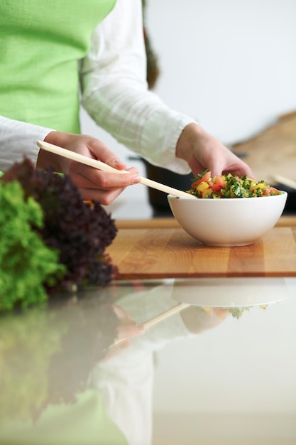 Gros plan sur des mains humaines faisant cuire une salade de légumes dans la cuisine sur la table en verre avec réflexion. Repas sain et concept végétarien