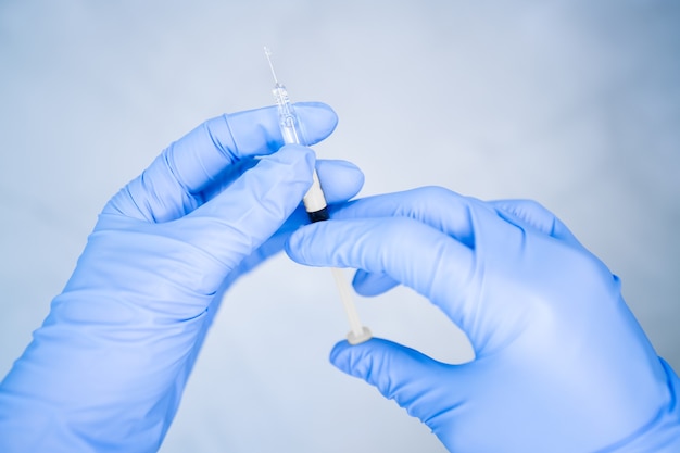 Gros plan des mains d'infirmière préparant le vaccin avec des gants bleus sur fond blanc