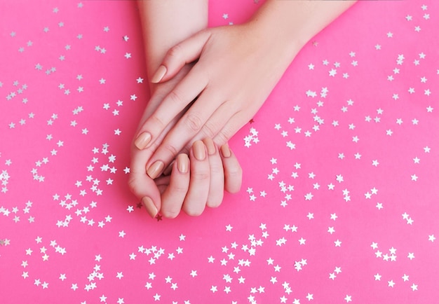 Gros plan des mains d'une jeune femme avec manucure sur les ongles sur fond rose