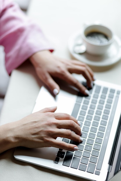 Gros plan des mains d'une jeune femme travaillant sur un ordinateur portable avec du café