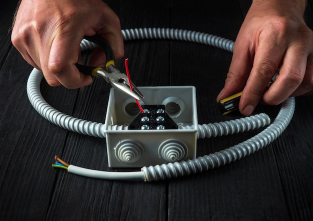 Photo gros plan des mains d'un maître électricien pendant le travail installation d'un câble ou d'un fil dans une boîte de jonction grise