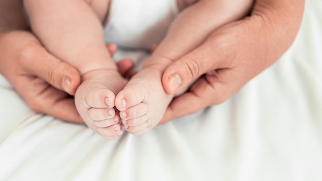 Gros plan sur les mains de maman tenant les pieds de bébé dans une pièce avec beaucoup de soleil