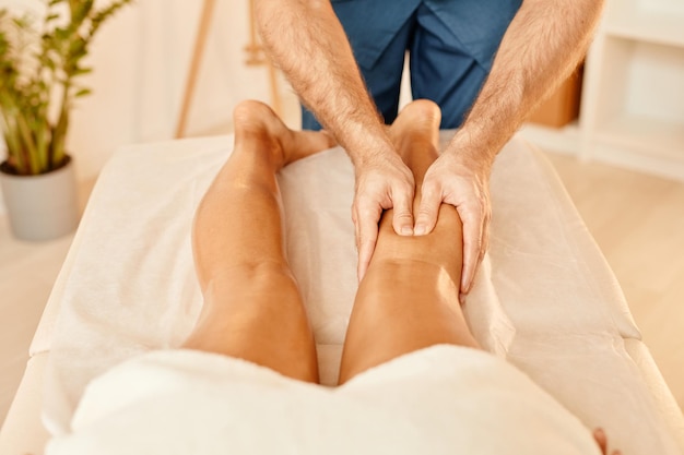 Gros plan des mains masculines massant les jambes sur la jeune femme dans l'espace de copie de la séance de spa