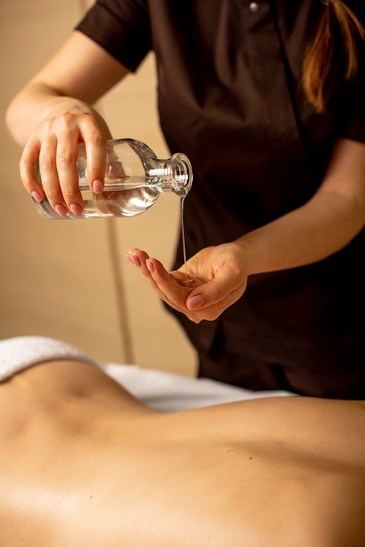 Photo gros plan des mains de masseur verser de l'huile d'arôme sur le dos de la femme