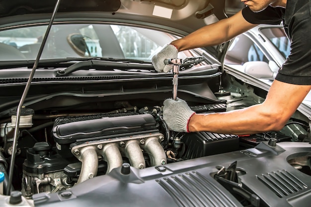 Gros plan des mains de mécanicien automobile utilisent la clé pour réparer et entretenir le moteur de voiture