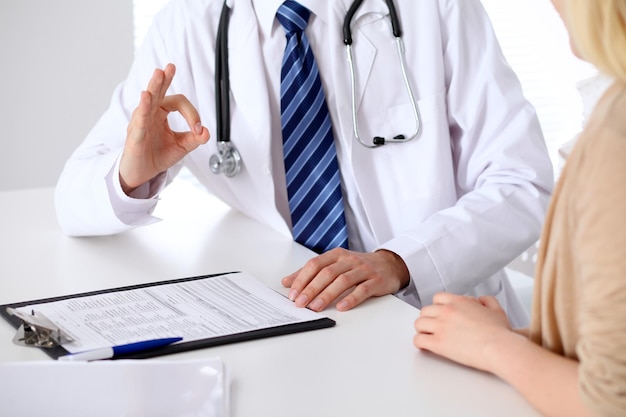 Gros plan sur les mains d'un médecin montrant un signe ok lors de la consultation d'un patient