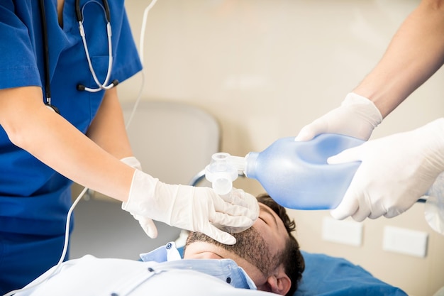 Gros plan sur les mains des médecins à l'aide d'un sac ambu pour réanimer un patient inconscient en salle d'urgence