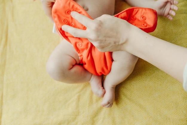 Gros plan des mains de la mère mettre une couche bébé orange à son nouveau-né