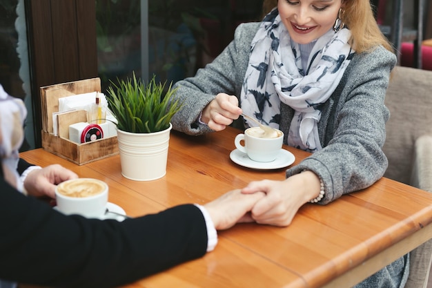 Gros plan sur les mains d'une mère et sa fille sur une table en bois dans un café. La mère et la fille adultes se tiennent la main et boivent du café.