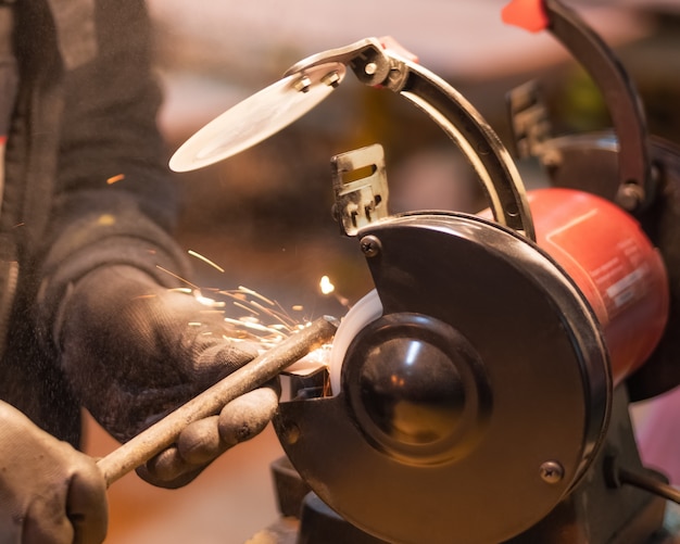 Gros plan des mains d'un ouvrier en gants noirs travaillant sur une pièce métallique sur une rectifieuse rouge