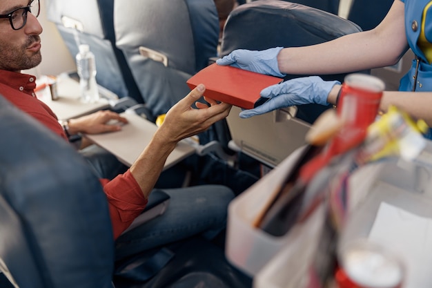 Gros plan sur les mains d'un passager masculin recevant une boîte à lunch d'une hôtesse de l'air servant de la nourriture à bord. Voyage, service, transport, concept d'avion