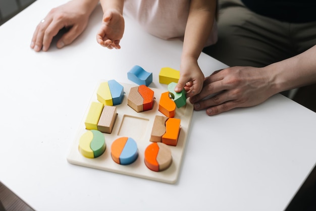 Photo gros plan des mains d'un père méconnaissable et de sa fille jouant avec des jouets en bois colorés à table