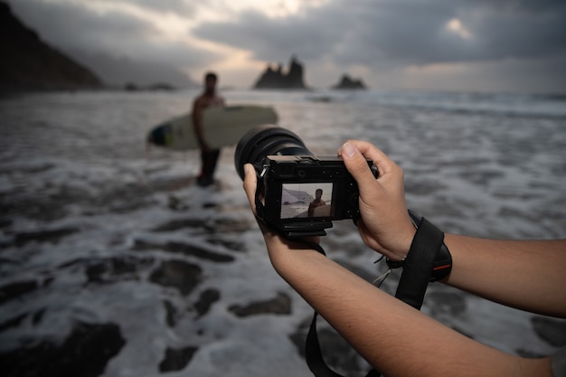 Gros plan des mains d'un photographe tenant son appareil photo lors d'une séance photo avec un surfeur