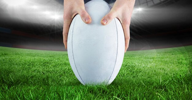 Photo gros plan des mains en plaçant un ballon de rugby sur gazon contre stade