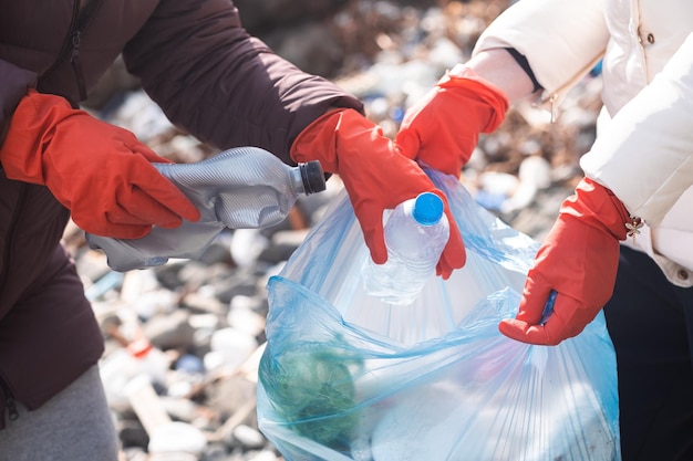 Gros plan sur des mains portant des gants ramassant des déchets plastiques pour aider à nettoyer l'environnement de la pollution