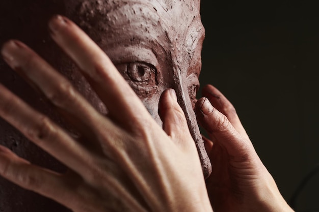 Gros plan de mains sculptant un vase en argile avec un visage