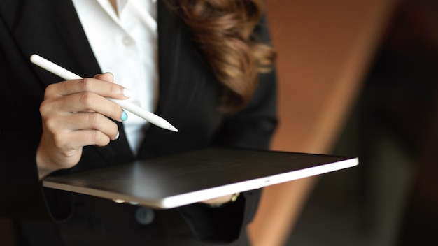 Gros plan sur les mains, tablette dans les mains d'une femme, travaillant via une tablette et tenant un stylet, employé de bureau