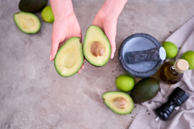 Gros plan sur les mains tenant un avocat frais coupé en deux sur une table en béton gris