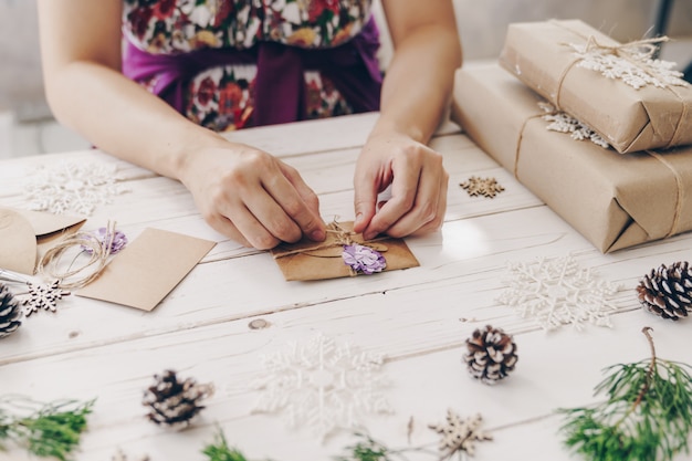 Gros plan des mains tenant la boîte-cadeau d'emballage et la carte de Noël sur une table en bois avec décoration de Noël.
