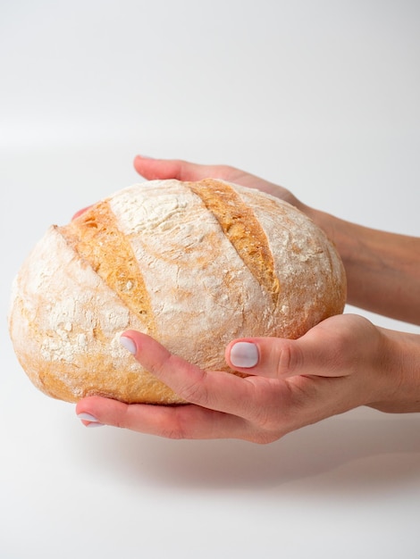 Gros plan des mains tenant un délicieux pain de blé rond frais et croustillant sur fond blanc