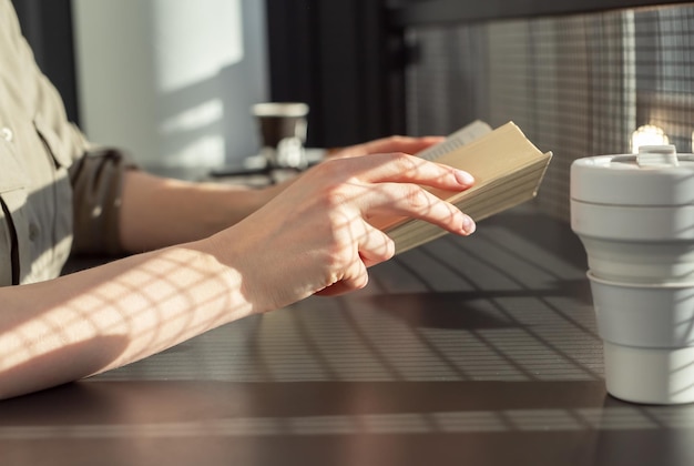 Gros plan sur les mains tenant un livre femme assise à une table de café et lisant un livre lisant de la littérature passe-temps con...