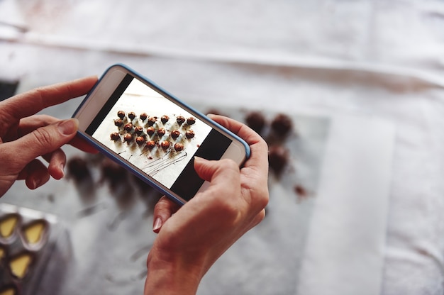 Gros plan des mains tenant le téléphone mobile et faire de la photographie de délicieux pralines au chocolat sur une nappe blanche. Téléphone mobile en régime de visualisation en direct. Fermer