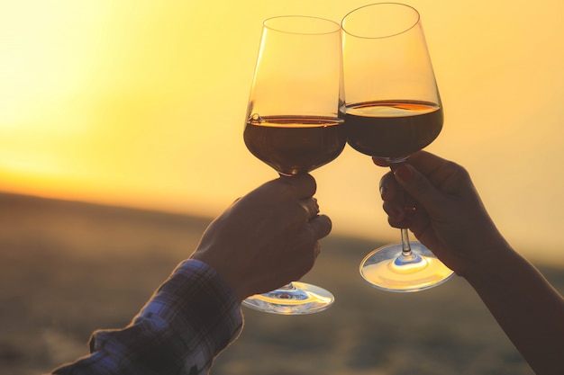 Gros plan sur les mains tenant des verres à vin rouges sur la plage pendant le coucher du soleil, concept de célébration