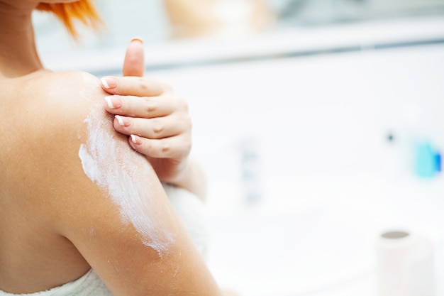 Gros plan des mains utiliser des produits de soins dans la salle de bain lumineuse.